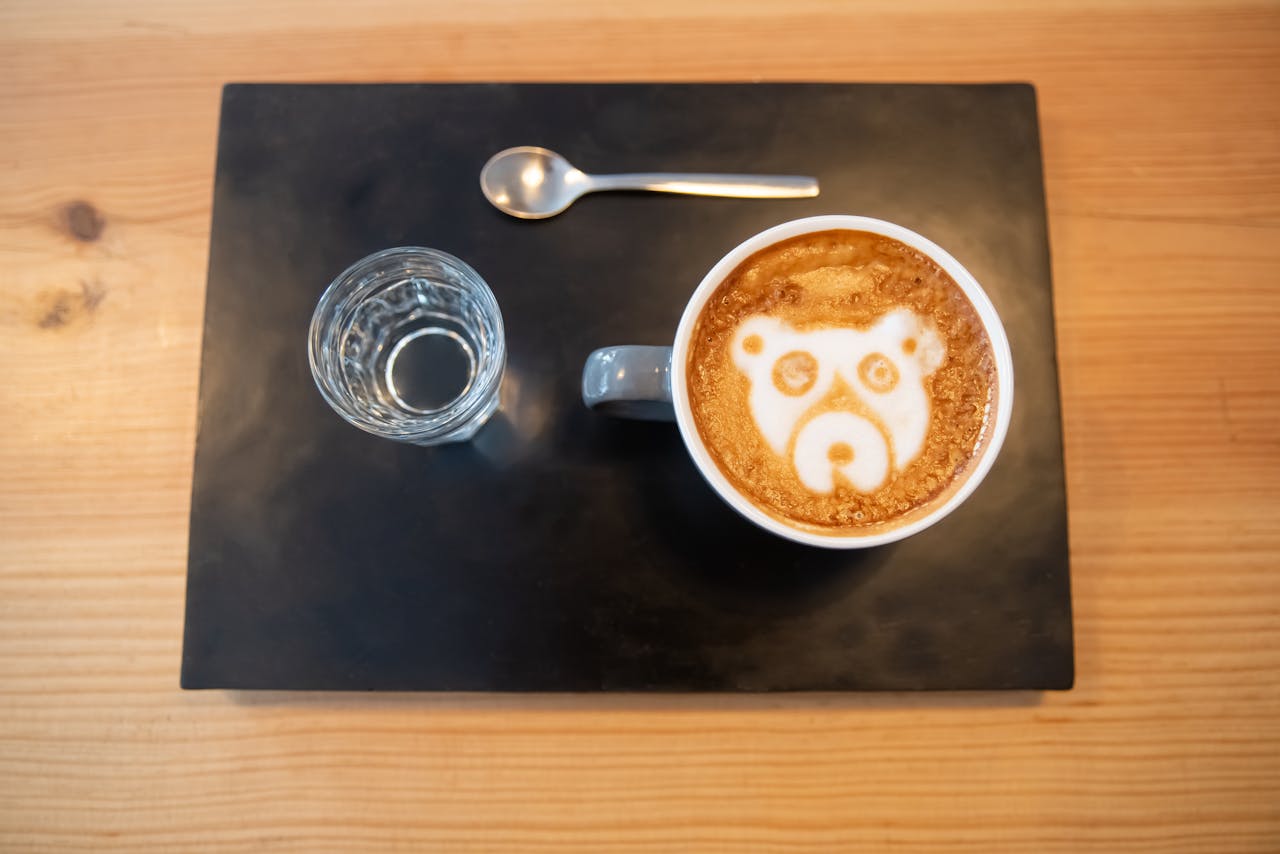 Top view of a latte with bear latte art, glass of water, and spoon on a tray.