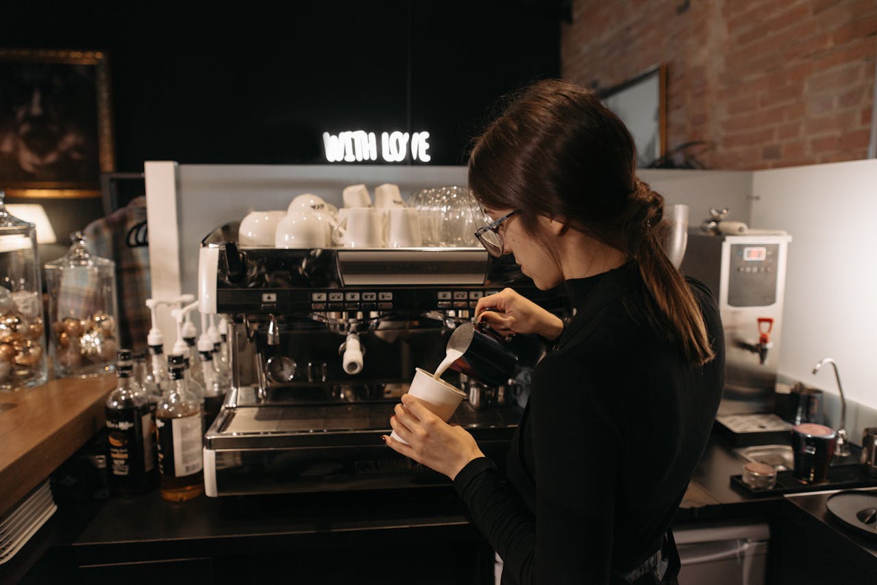 Barista skillfully pours milk while preparing coffee in a cozy café.